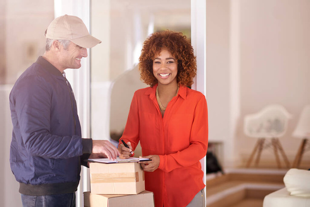 Signed sealed delivered. a young woman receiving a package and signing it while looking at the camera in her home - Photo, Image