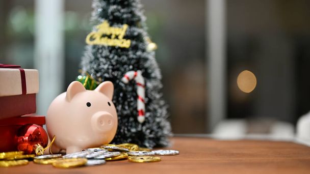 close-up image, small Christmas tree with piggy bank, coins and gift box on wood table. Christmas holiday concept - 写真・画像