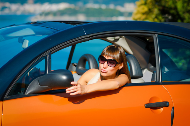 Mooie jonge vrouw met lange haren kijken in de spiegel in oranje cabriolet aan de Middellandse Zeekust  - Foto, afbeelding