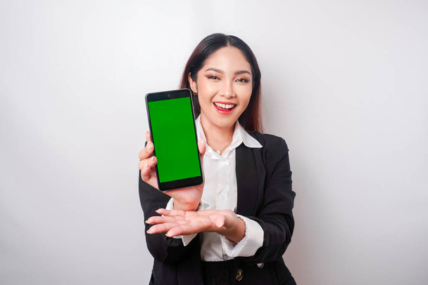 Mutlu genç bir iş kadını siyah takım elbise giyiyor, telefonunda beyaz arka planla izole edilmiş fotokopi alanı gösteriyor. - Fotoğraf, Görsel