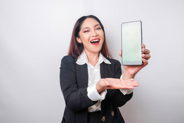 Eine glückliche junge Geschäftsfrau trägt einen schwarzen Anzug und zeigt Kopierraum auf ihrem Handy, isoliert von weißem Hintergrund - Foto, Bild