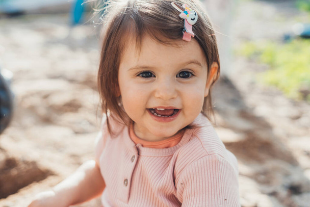 Ritratto ravvicinato di una adorabile bambina che sorride alla telecamera mentre gioca all'aperto in estate. Ragazzo che gioca nel parco giochi trascorrendo del tempo nei giochi - Foto, immagini