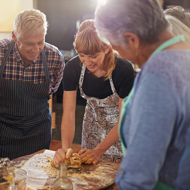 Mostrando loro come fare l'impasto perfetto. un gruppo di anziani che frequentano un corso di cucina - Foto, immagini