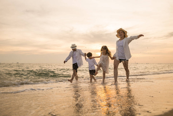 Tropical summer vacations, Happy family having fun running on a sandy beach at sunset time, People of father, mother, children son and daughter family of four holding hands together walking on beach - Fotografie, Obrázek