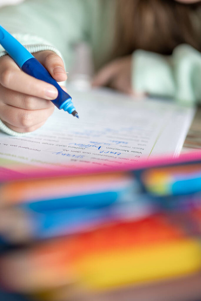  child writes with a pencil in a notebook.Close-up pencil in a childs hand. Homework.Girl in a green sweatshirt writes words in a notebook.Study and education concept.schoolgirl does her homework. - 写真・画像