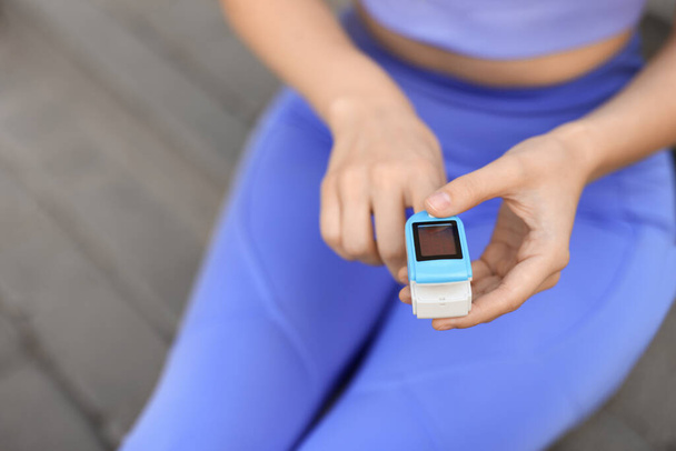 Woman checking pulse with blood pressure monitor on finger after training outdoors, closeup. Space for text - Foto, Bild