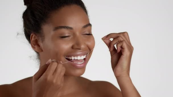 Głęboka higiena jamy ustnej. Close up portret szczęśliwej african amerykańskiej kobiety nici dentystycznej zębów z nici dentystycznej, białe tło studio, zwolnione tempo, puste miejsce - Materiał filmowy, wideo