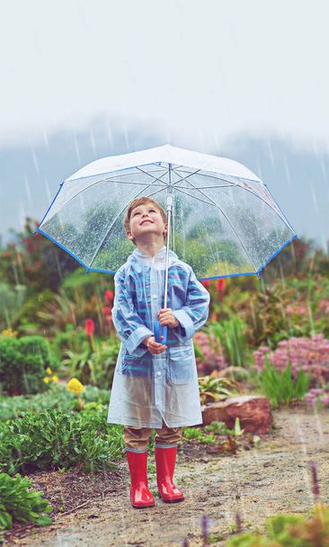 Στον κήπο μου αρέσει η βροχή. Όλο το μήκος πλάνο ενός νεαρού αγοριού στέκεται έξω στη βροχή - Φωτογραφία, εικόνα