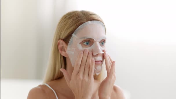 Ochtendschoonheidsrituelen. close-up portret van blonde vrouw van toepassing verwennerij voedende gezichtsmasker op gezicht, kijken opzij thuis, slow motion, vrije ruimte - Video