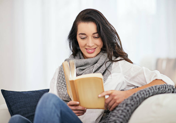 Nos perdemos en los libros, nos encontramos allí también. una joven leyendo un libro mientras está sentada en la sala - Foto, Imagen