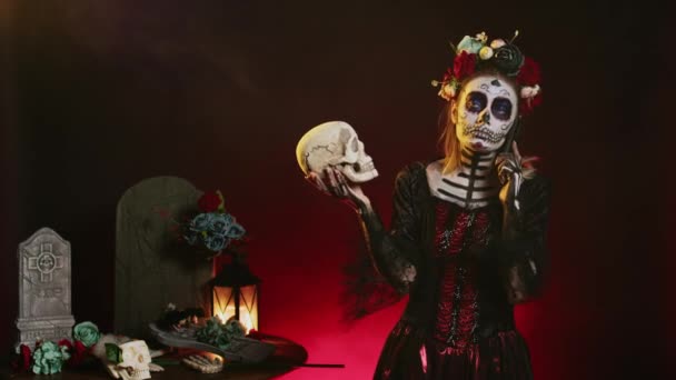 Santa muerte model on phone call holding skull, talking on smartphone line and acting creepy in studio. Answering telephone for remote chat, wearing holy mexican goddess costume. - Footage, Video