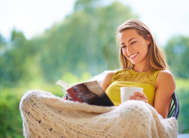 Everything gets better with coffee. a young woman reading a book at home - Foto, imagen