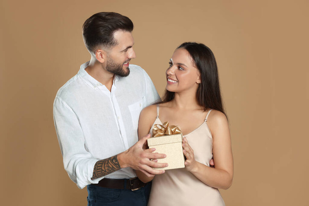 Lovely couple with gift on beige background - Zdjęcie, obraz