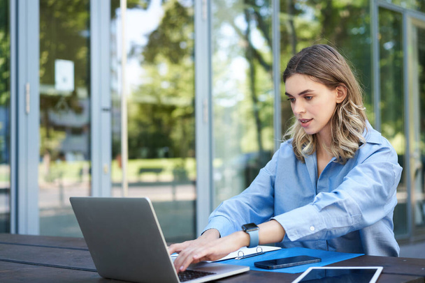 Empresária bem sucedida trabalhando ao ar livre, sentada no ar fresco com laptop, documentos e papéis, olhando para a tela do computador. - Foto, Imagem