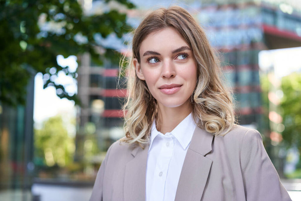 Portrait of young successful businesswoman in suit, cross arms on chest, smile and look confident, standing on street of business center. - Photo, Image