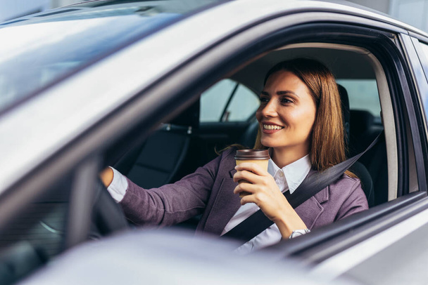 Fiatal üzletasszony vezet autóval dolgozni a nap folyamán, kávét iszik. - Fotó, kép