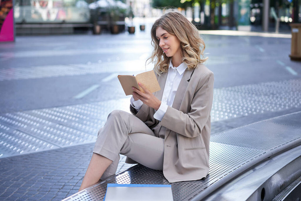 Femme travaillant, écrivant des pensées dans son planificateur, assise dans le centre-ville en vêtements d'affaires. - Photo, image