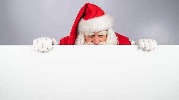 Le Père Noël jette un coup d'oeil derrière une annonce sur un fond blanc. Joyeux Noël - Photo, image