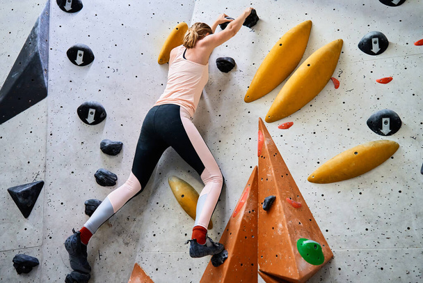 Женщина забирается на стену в боулдеринговом зале. Тренировка альпинистки, висит на стене для скалолазания. Концепция активного образа жизни и экстремального спорта. - Фото, изображение