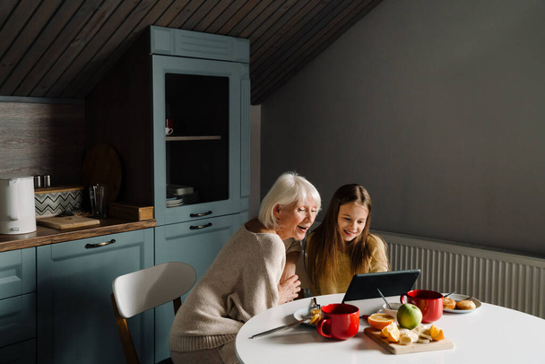 Senior woman and her granddaughter using tablet computer while having breakfast at home - Foto, Bild