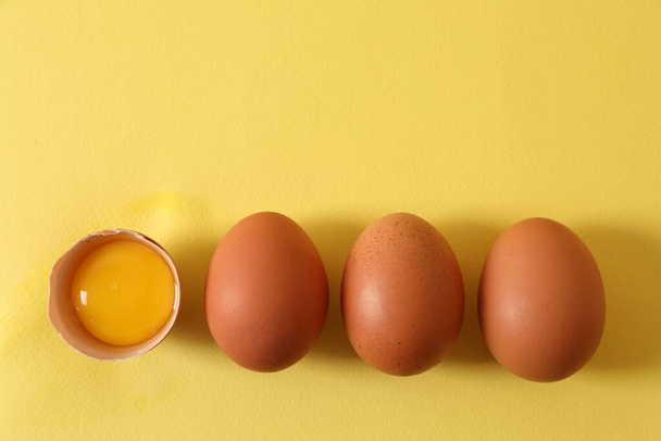 Cracked and whole chicken eggs on yellow background, flat lay. Space for text - Photo, Image