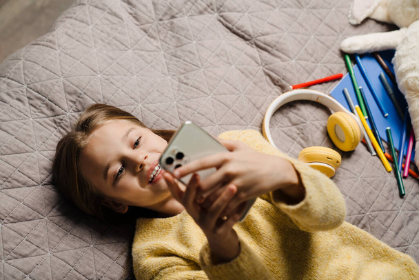 White happy girl using mobile phone while lying on bed at home - Φωτογραφία, εικόνα