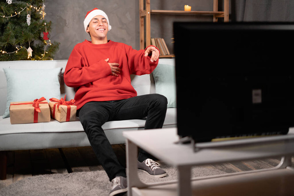 若い男はクリスマスに自宅でソファの上でテレビを見て素敵な肯定的な明るい陽気な陽気な陽気。スペースのコピー - 写真・画像