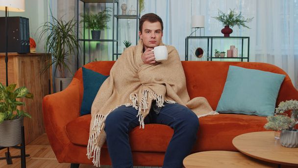 Hasta öğrenci kanepede soğuktan titreyerek ekoseye sarılmış, ısınmamış odada sıcak çay içiyor borç krizi olmadan. Rahatsız hisseden sağlıksız genç adam ısınmaya çalışıyor. Kış Zamanı - Fotoğraf, Görsel