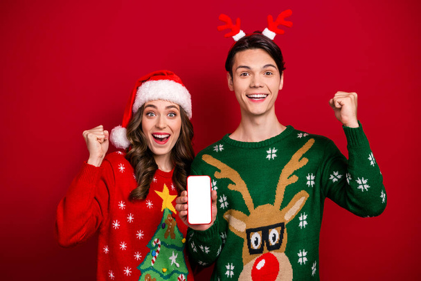 Photo of two excited funny people raise fists showing empty space telephone display isolated on red color background. - 写真・画像