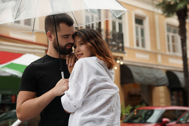 Young couple with umbrella enjoying time together under rain on city street - Zdjęcie, obraz