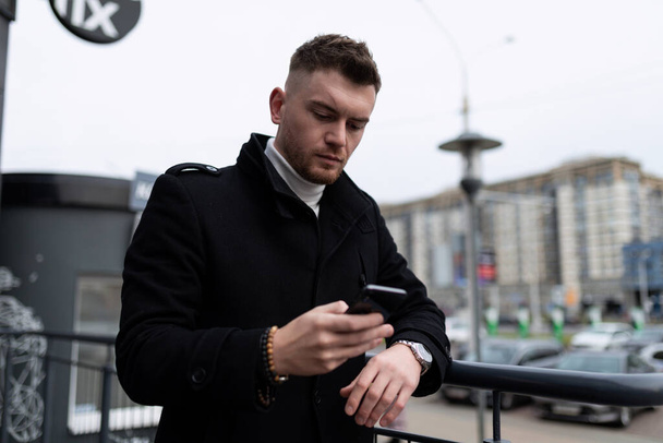 jeune homme en vêtements de travail avec un téléphone portable dans ses mains à l'extérieur. - Photo, image