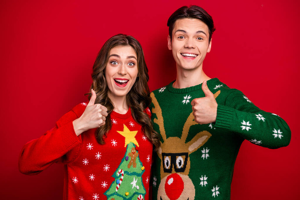 Photo of pretty excited best friends dressed x-mas jumpers showing thumbs up isolated red color background. - Foto, afbeelding