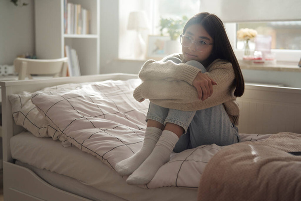 Pensive valkoihoinen teini tyttö istuu sängyllä ja katselee pois - Valokuva, kuva