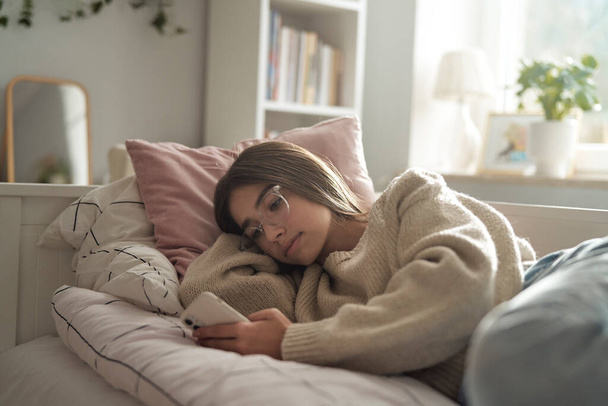Caucasian teenage girl browsing phone while lying on bed - Foto, Imagem