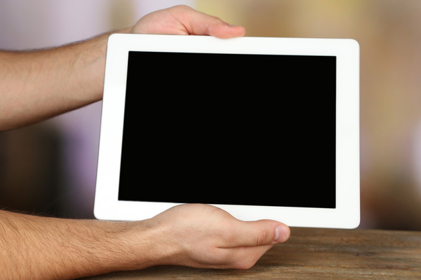 Manos sosteniendo la tableta PC sobre mesa de madera y fondo borroso claro
 - Foto, Imagen