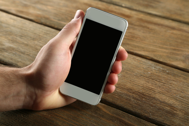 Hand holding smart mobile phone on wooden table background - Fotó, kép