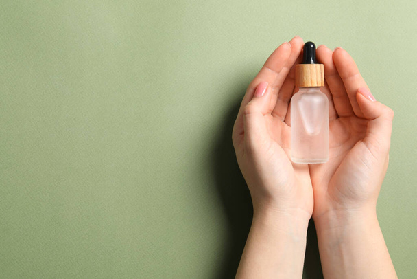 Woman holding bottle with serum on olive background, top view. Space for text - Fotoğraf, Görsel