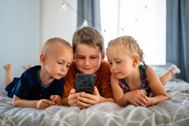 Portrait of children having fun, playing on mobile phone together at home. Internet and network addiction. - Foto, Imagen