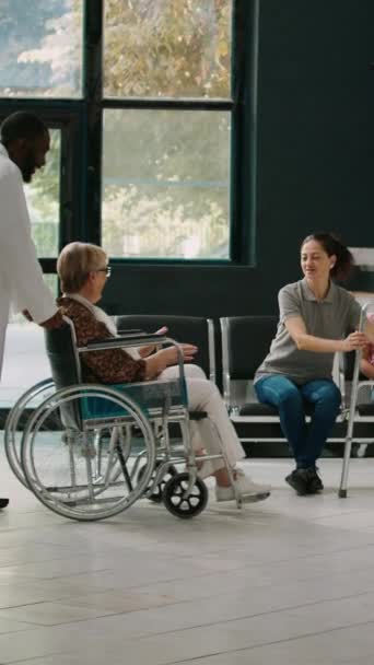 Vidéo verticale : Vieil adulte en fauteuil roulant parlant à un jeune enfant dans une salle d'attente, famille venant rendre visite à un patient âgé ayant une déficience. Utilisateur de fauteuil roulant essayant de marcher avec cadre de marche à l'hôpital - Séquence, vidéo