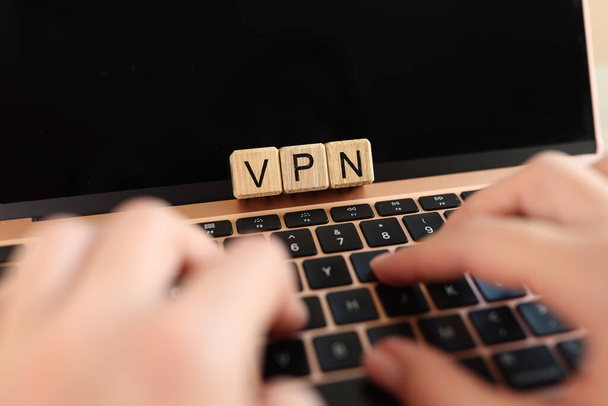 Internet user works on laptop with VPN Virtual Private Network for secure and encrypted connection, anonymously on Internet. Hands on laptop keyboard and letters VPN on cubes. - Photo, Image