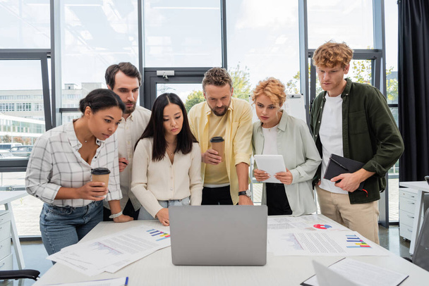 multietnikus üzleti csapat nézi laptop közelében papírok grafikonok konferenciaasztalon - Fotó, kép