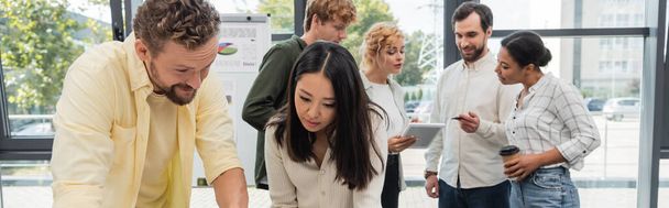brunette asian woman near bearded colleague and business team talking on background, banner - Foto, Imagen