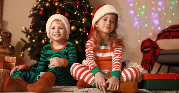 Petits enfants mignons dans les chapeaux et pyjamas du Père Noël à la maison la veille de Noël  - Photo, image