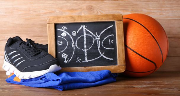 Chalkboard with drawn scheme of basketball game, sportswear and ball on wooden background - Photo, Image