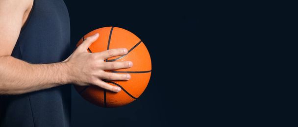 Male basketball player holding ball on dark background with space for text, closeup - Fotografie, Obrázek