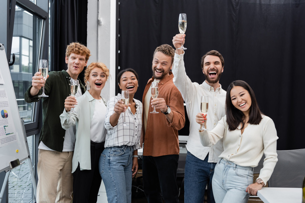 Excited multicultural business people rising glasses of champagne in office  - Photo, image