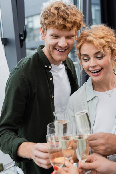 Smiling redhead businessman in casual clothes clinking champagne with colleagues in office  - Photo, Image