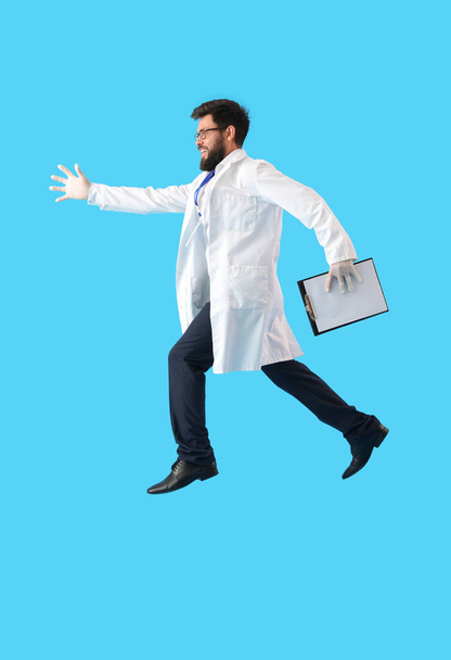 Male doctor with clipboard jumping on blue background - Photo, image