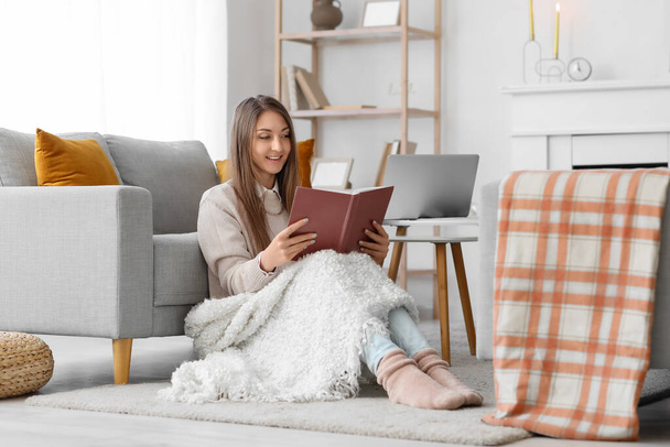Jeune femme avec livre de lecture à carreaux chaud à la maison - Photo, image