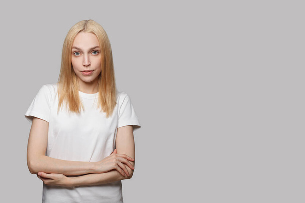 Kaunis nuori nainen valkoisessa t-paidassa seisoo ristissä kädet valkoisella bannerin taustalla - Valokuva, kuva